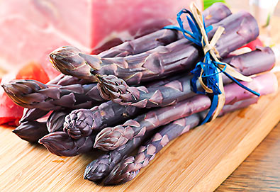 A bundle of 9 Purple Passion asparagus shoots tied with blue and beige paper ribbon atop a bamboo cutting board